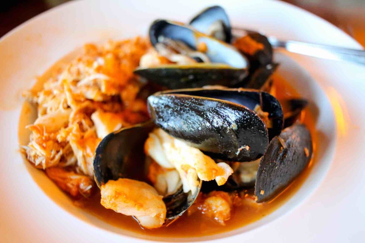 a white bowl full of crab meat and cooked mussels with a red sauce (probably made from crab shells and wine) 