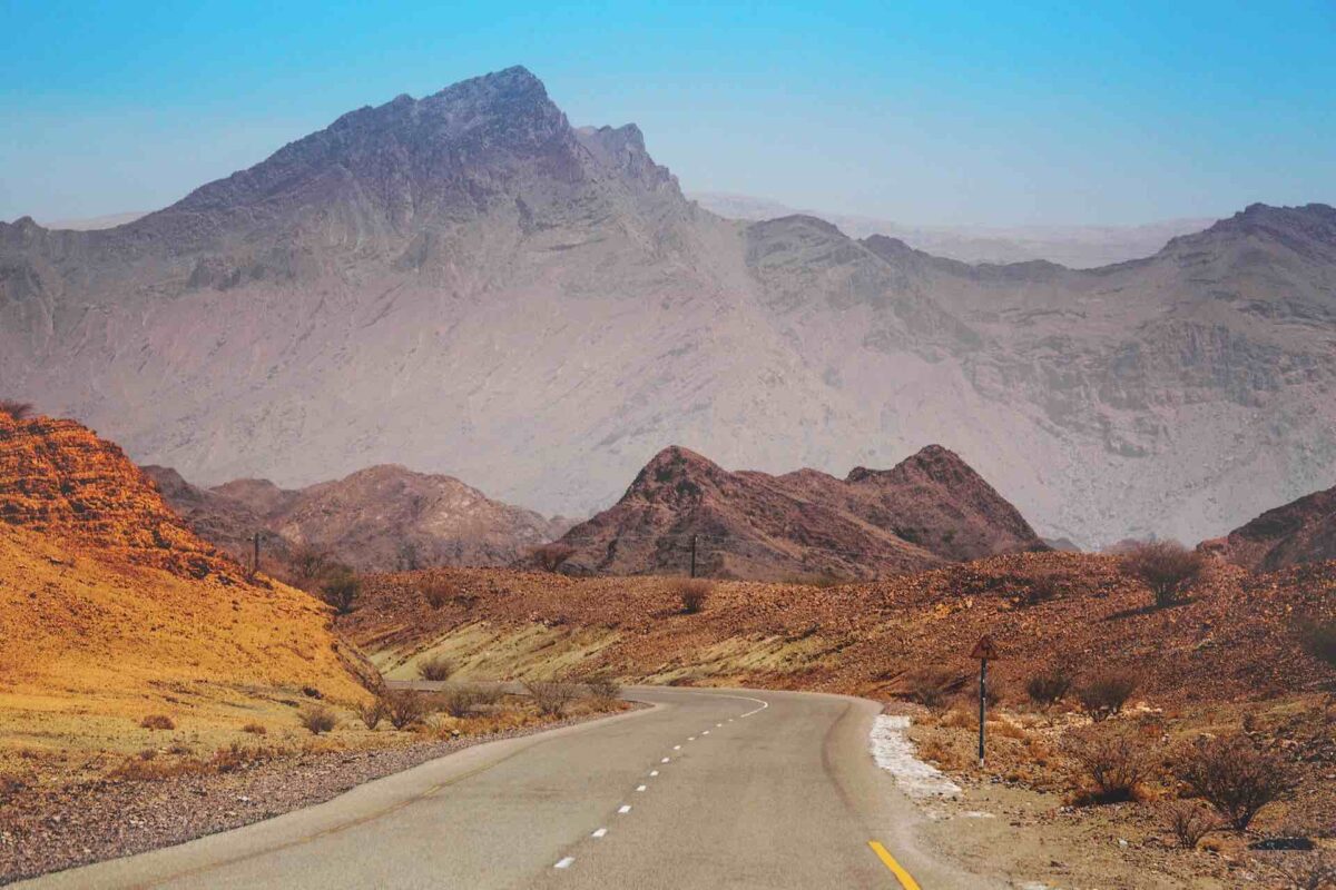 mountains in the background, barren landscape of Oman and a dual road curving around the mountains in the distant (blue sky above the mountains)